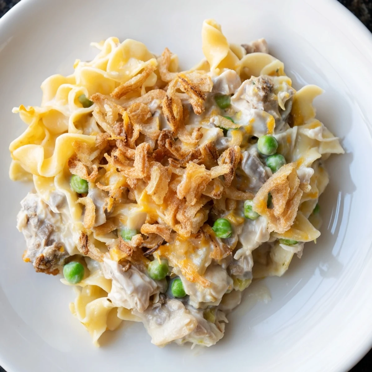 A close-up shot of a bubbling creamy tuna noodle casserole with a crispy onion topping.