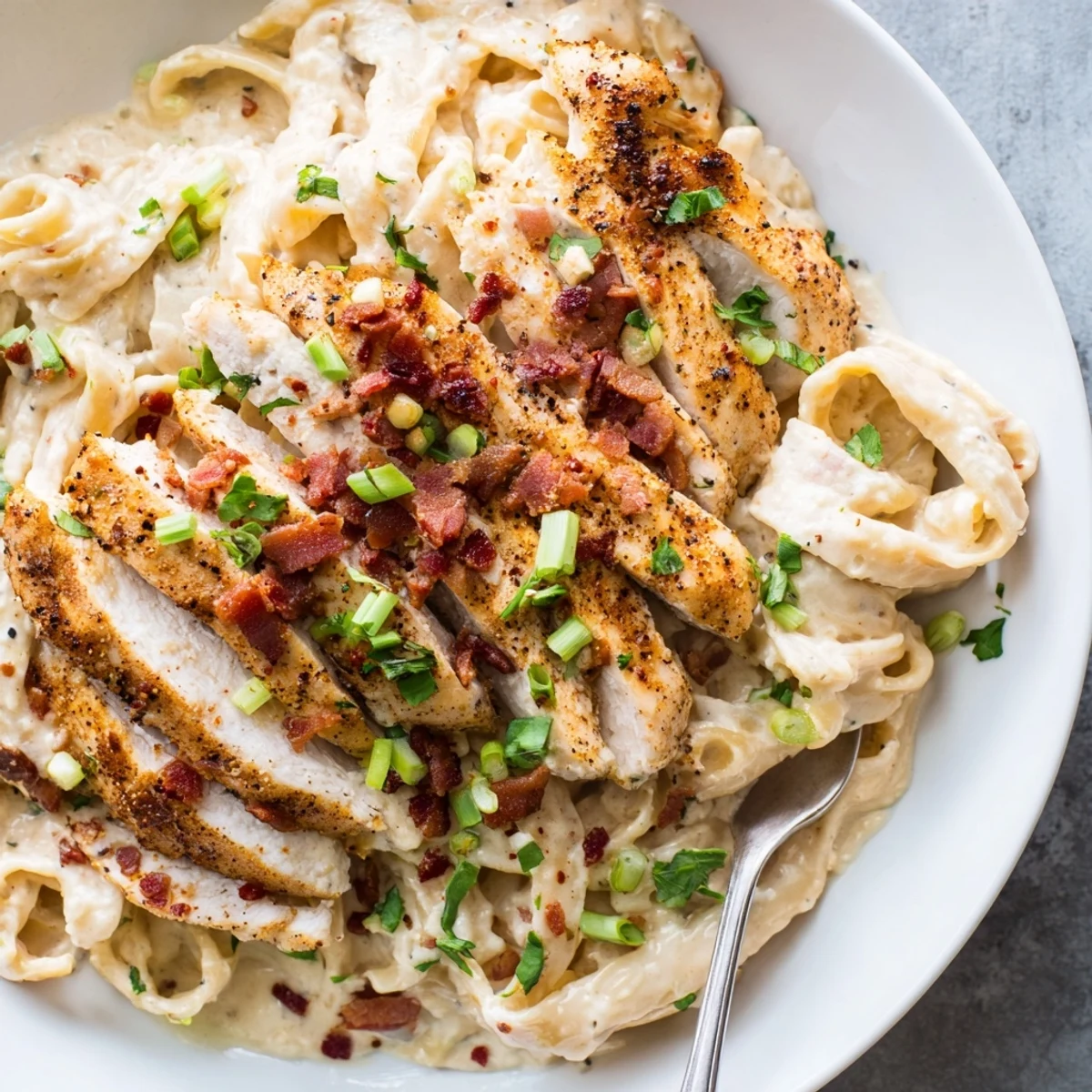 Creamy parmesan sauce blankets the Southern Style Creamy Parmesan Chicken Pasta, topped with fresh herbs and crumbled bacon.