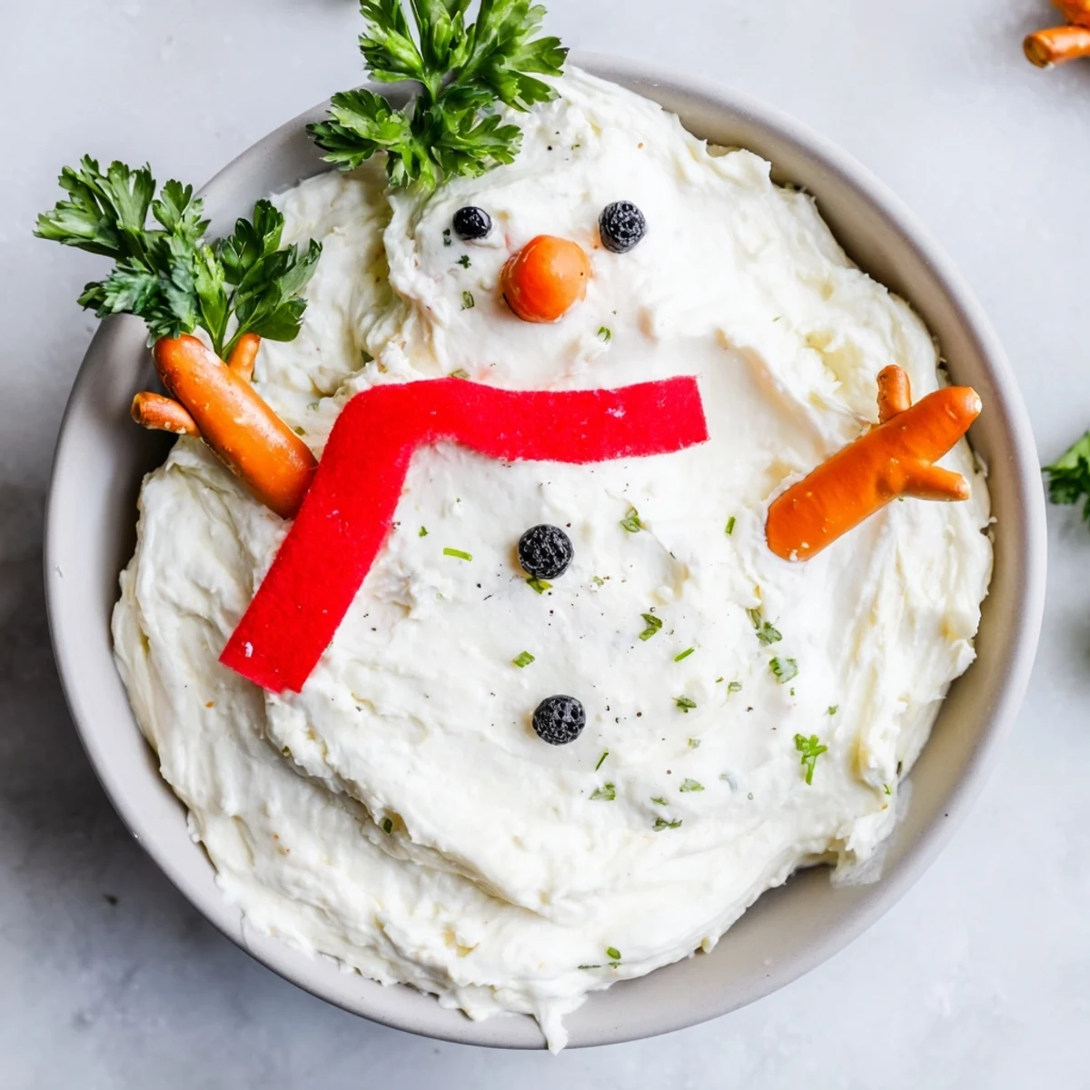 Festive Melted Snowman Dip, a holiday dip with a bright orange carrot nose and tasty black olive eyes.
