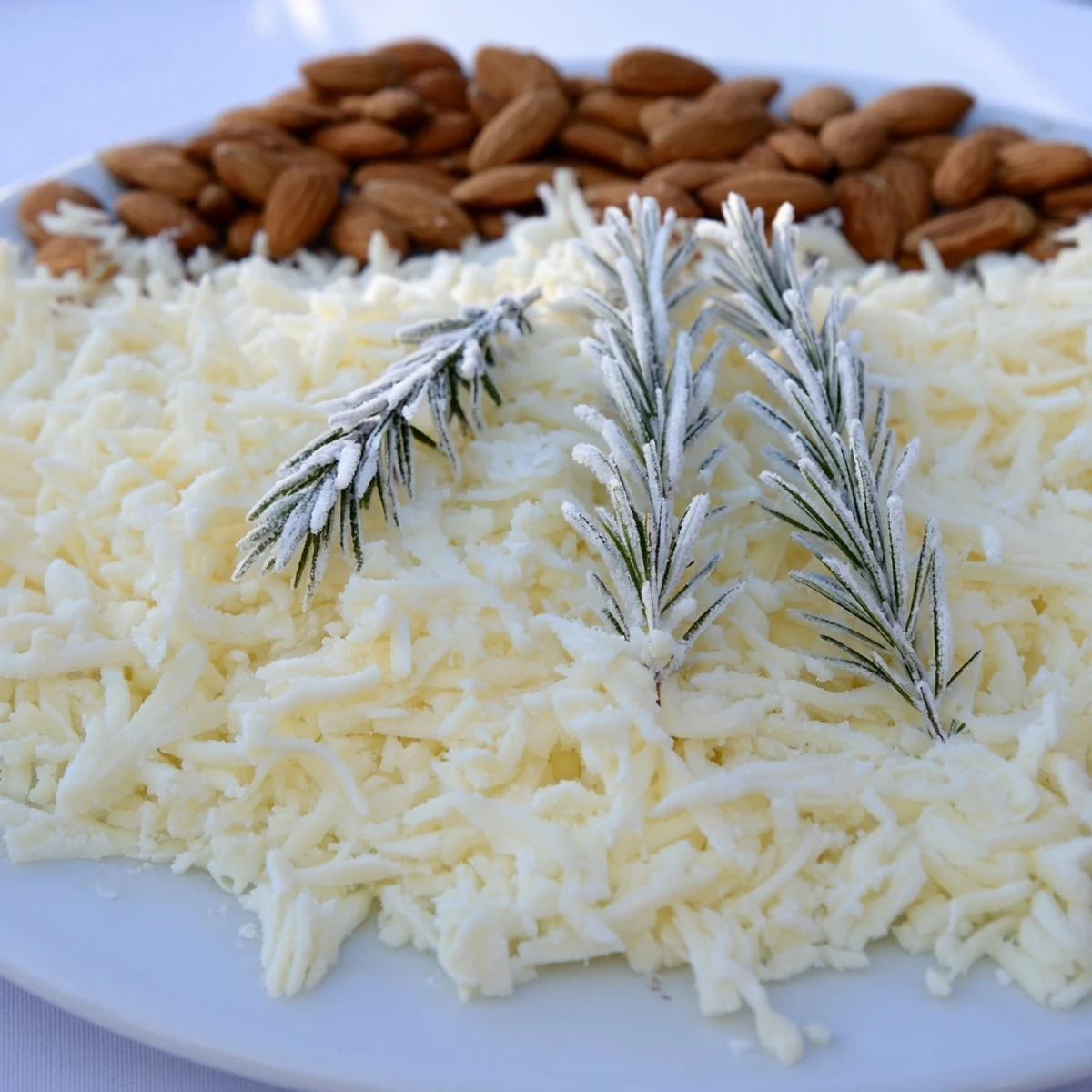 A festive cheese platter titled "The Frosted Pine," featuring sugared rosemary and white cheddar.