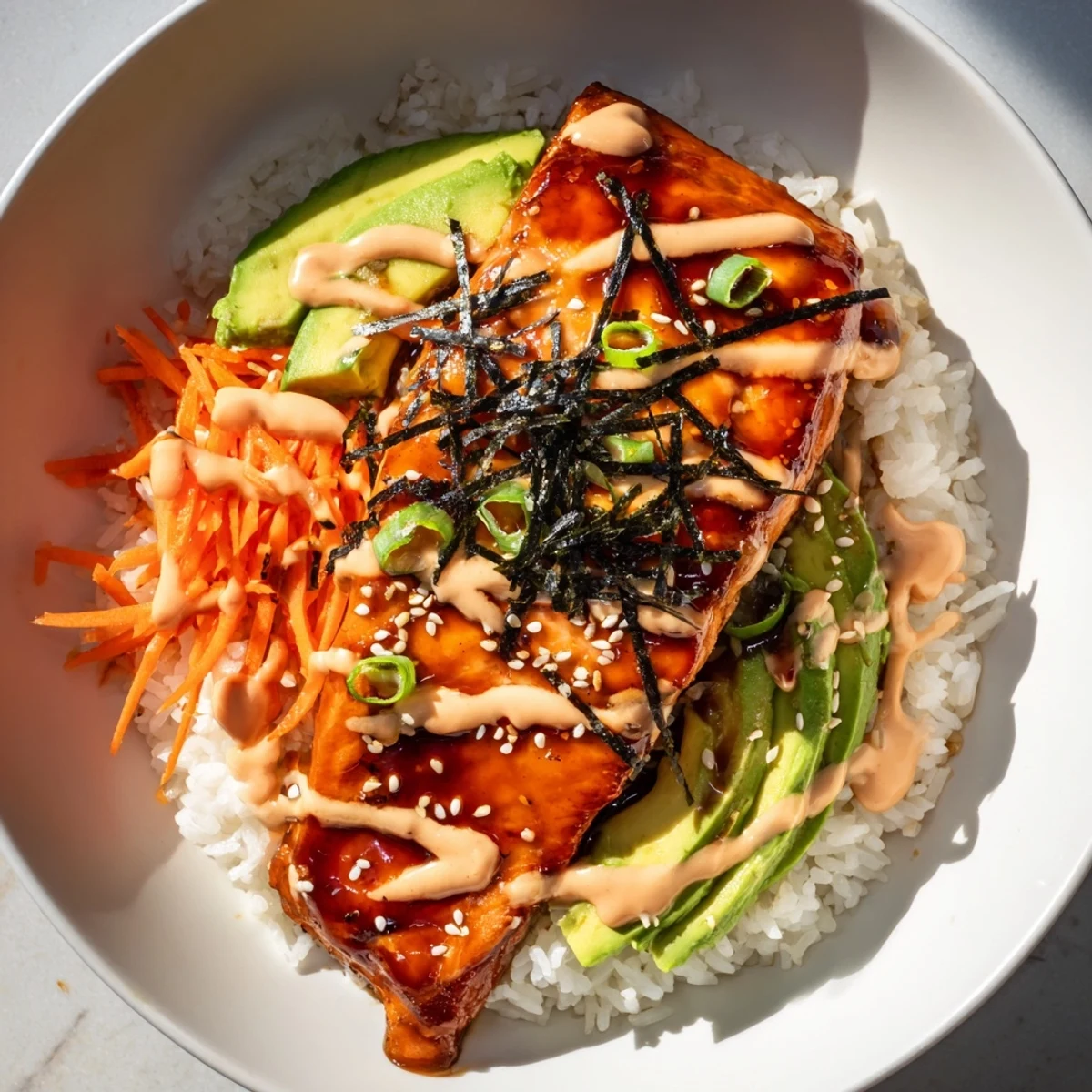 This teriyaki salmon rice bowl features shiny, glistening salmon resting atop fluffy white rice and fresh avocado.