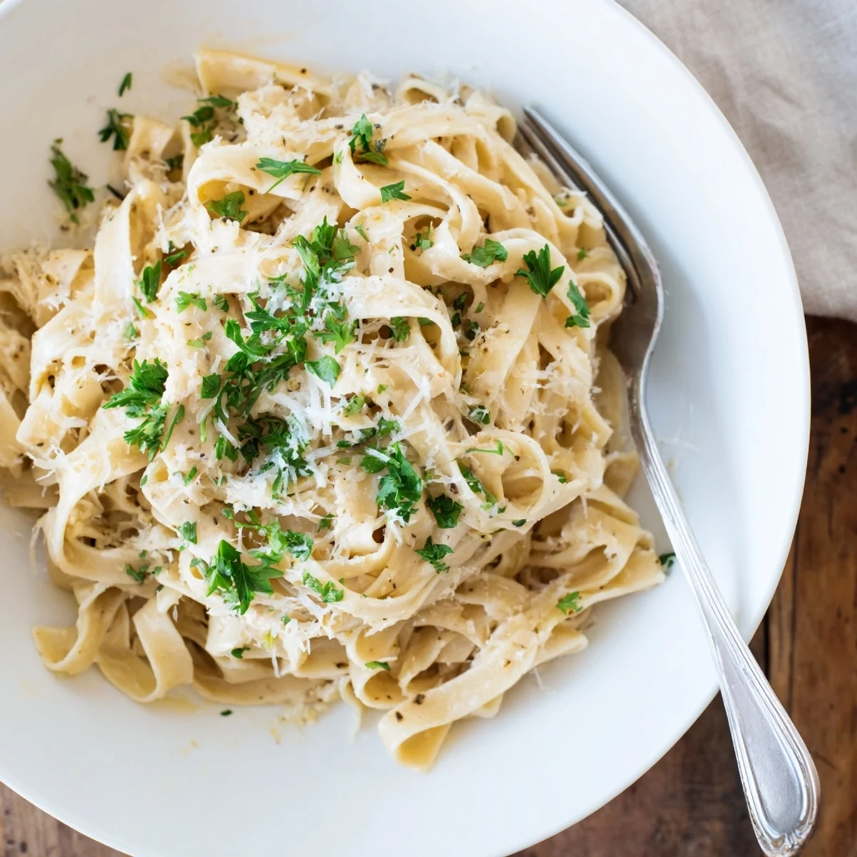 Plate of roasted garlic cream pasta next to fresh parsley and a glass of Pinot Grigio. 