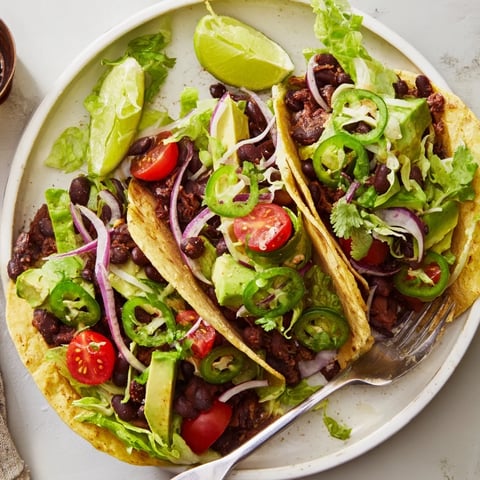 Fresh avocado and black bean tacos topped with vibrant veggies and lime wedges.  