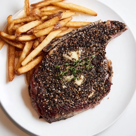 Juicy Classic Peppercorn Ribeye glistening with peppercorns, alongside a pile of golden-brown crispy fries.