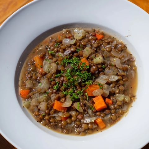 Steaming bowl of Lentil Soup with carrots and celery, garnished with fresh parsley, ready to eat.