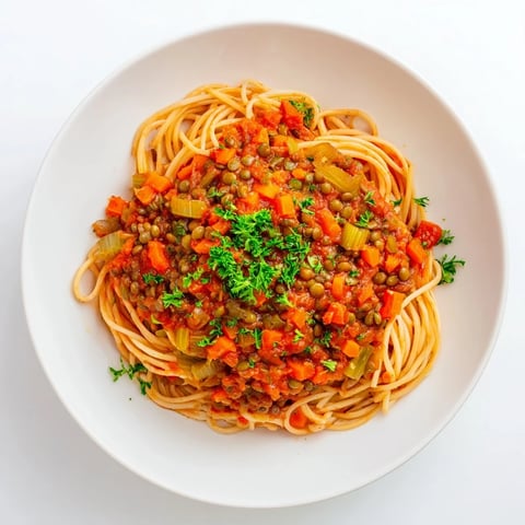 Steaming bowl of Hearty Lentil Bolognese, a rich vegan pasta dish, topped with fresh parsley.