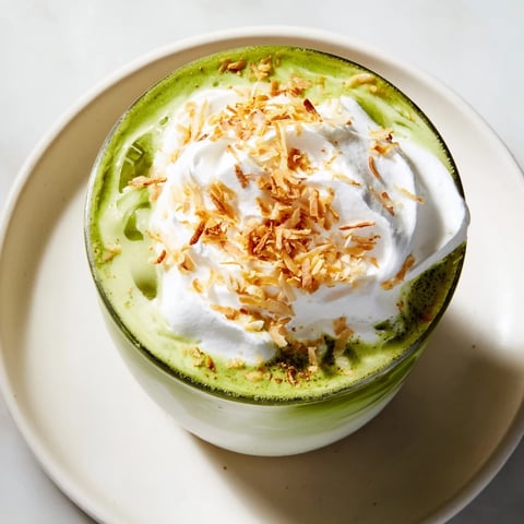 Steaming, creamy toasted coconut gingerbread iced matcha garnished with whipped cream, ready to enjoy.