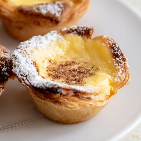 Golden, bubbly Portuguese egg tarts with a dusting of cinnamon, perfect for a sweet treat.