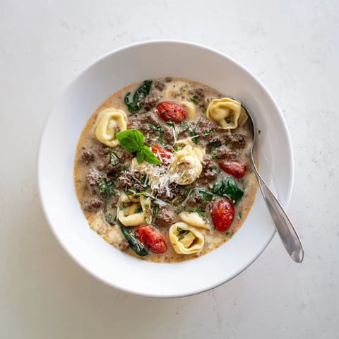Tortellini Beef Soup in a white bowl garnished with Parmesan and fresh basil leaves.  