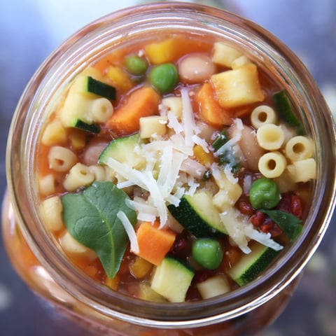 Brightly layered Minestrone Soup in a jar, showcasing vibrant diced carrots, celery, zucchini, and red lentils packed for a nourishing grab-and-go meal.