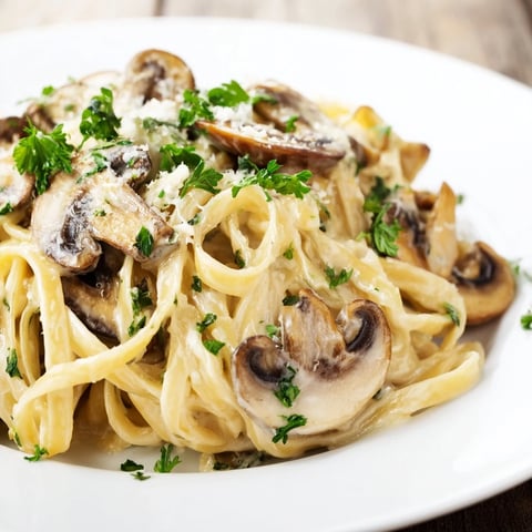 Steaming fettuccine glistening with creamy mushroom Alfredo sauce, topped with fresh parsley on a rustic table.