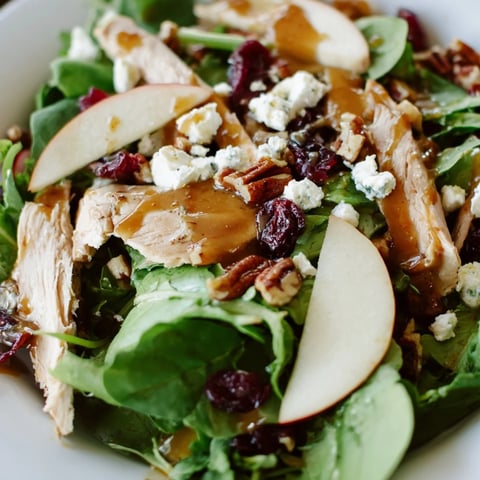 Sliced chicken and crisp apples over mixed greens, topped with a caramel-pecan dressing on a white platter.