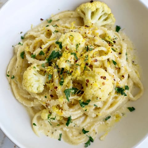 A bowl of Creamy Roasted Cauliflower Garlic Pasta, topped with fresh herbs and parmesan cheese.