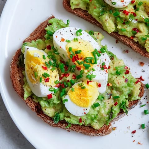 A close-up of creamy avocado egg smash, with soft herbs and served on whole-grain toast.