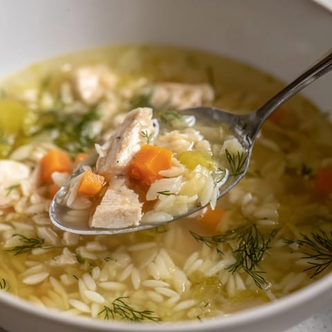 Close-up of vibrant Chicken Lemon Orzo Soup with tender chicken, carrots, and orzo pasta in a rich broth.