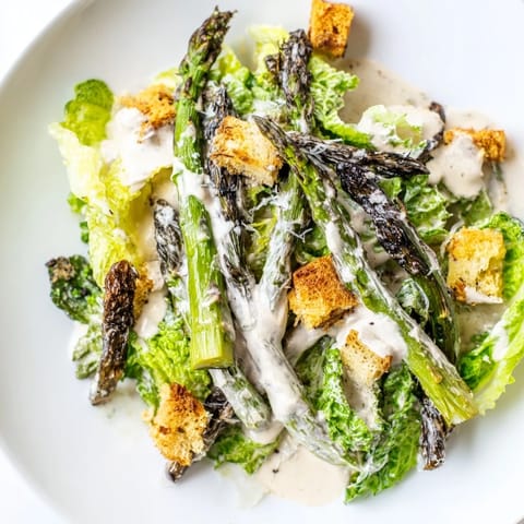 Charred asparagus spears glisten over crisp romaine lettuce in this Roasted Asparagus Caesar Salad, topped with golden croutons and shaved Parmesan.