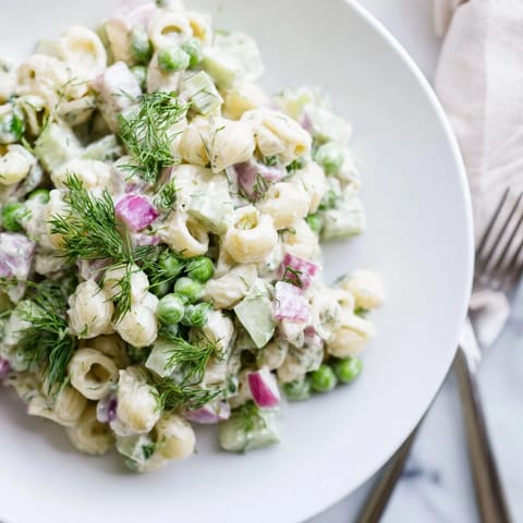 Tangy creamy dill pickle pasta salad with vibrant green peas and chopped dill pickles, served chilled on a rustic wooden table.  