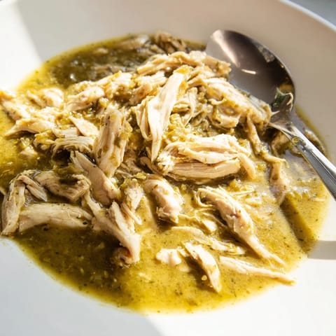 A rustic Dutch oven holds bubbling Chicken Chili Verde, featuring charred peppers and tomatillos, garnished with creamy avocado slices.