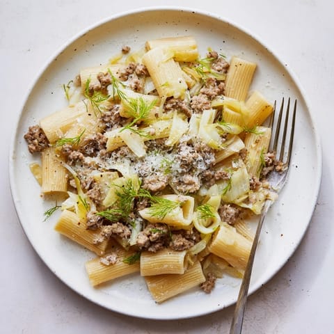 A close-up of Winter Pasta with Sausage and Fennel, featuring glossy sauce, fresh fennel fronds, and a generous sprinkle of Parmesan cheese.