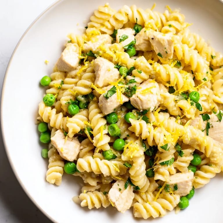 This hearty Garlic Butter Chicken & Pea Pasta is plated with a light sprinkle of Parmesan, ready for a family dinner.