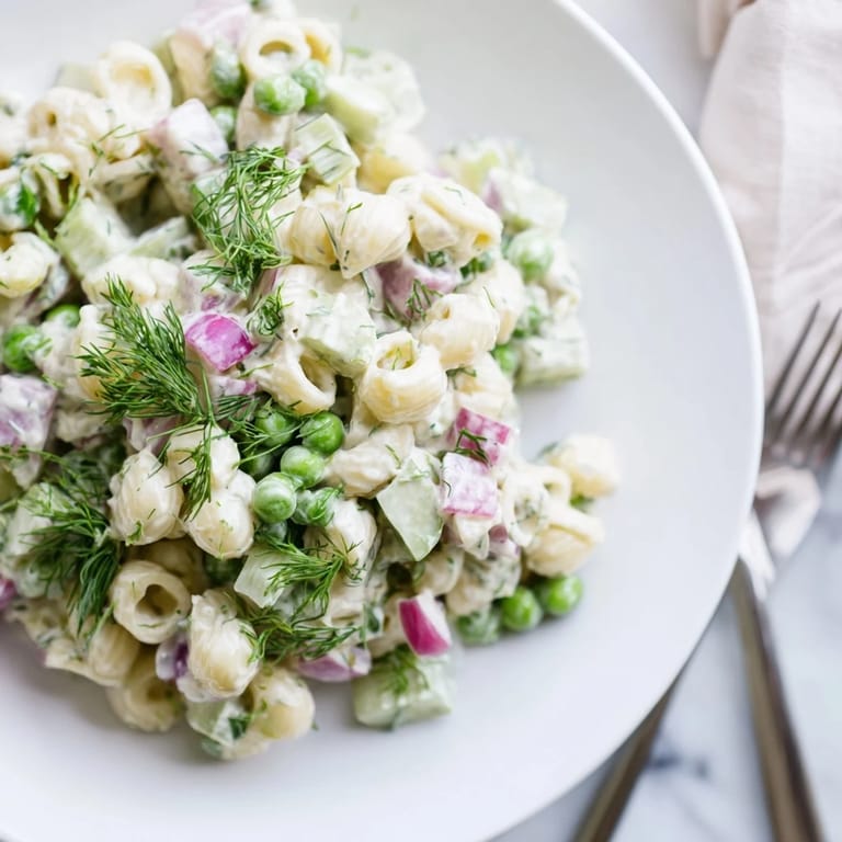 Tangy creamy dill pickle pasta salad with vibrant green peas and chopped dill pickles, served chilled on a rustic wooden table.  