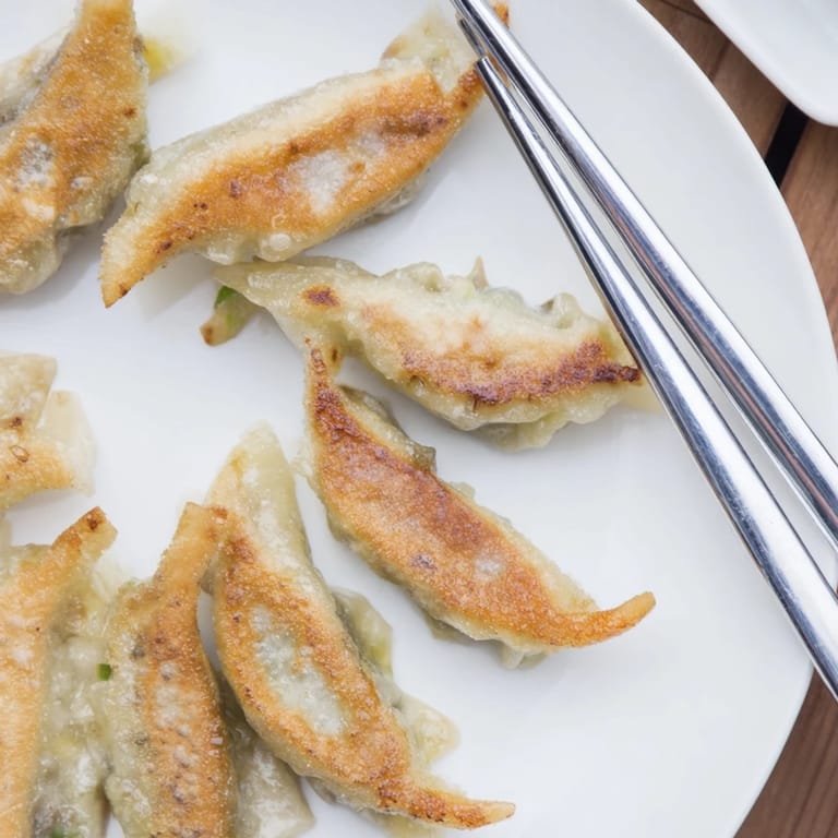 Homemade smashed gyozas arranged neatly, perfect for dipping in spicy chili oil and sesame seeds.