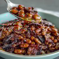 A close-up of a bubbling casserole dish filled with Summer BBQ Baked Beans, showcasing tender beans in a rich, sweet sauce topped with crispy bacon pieces.
